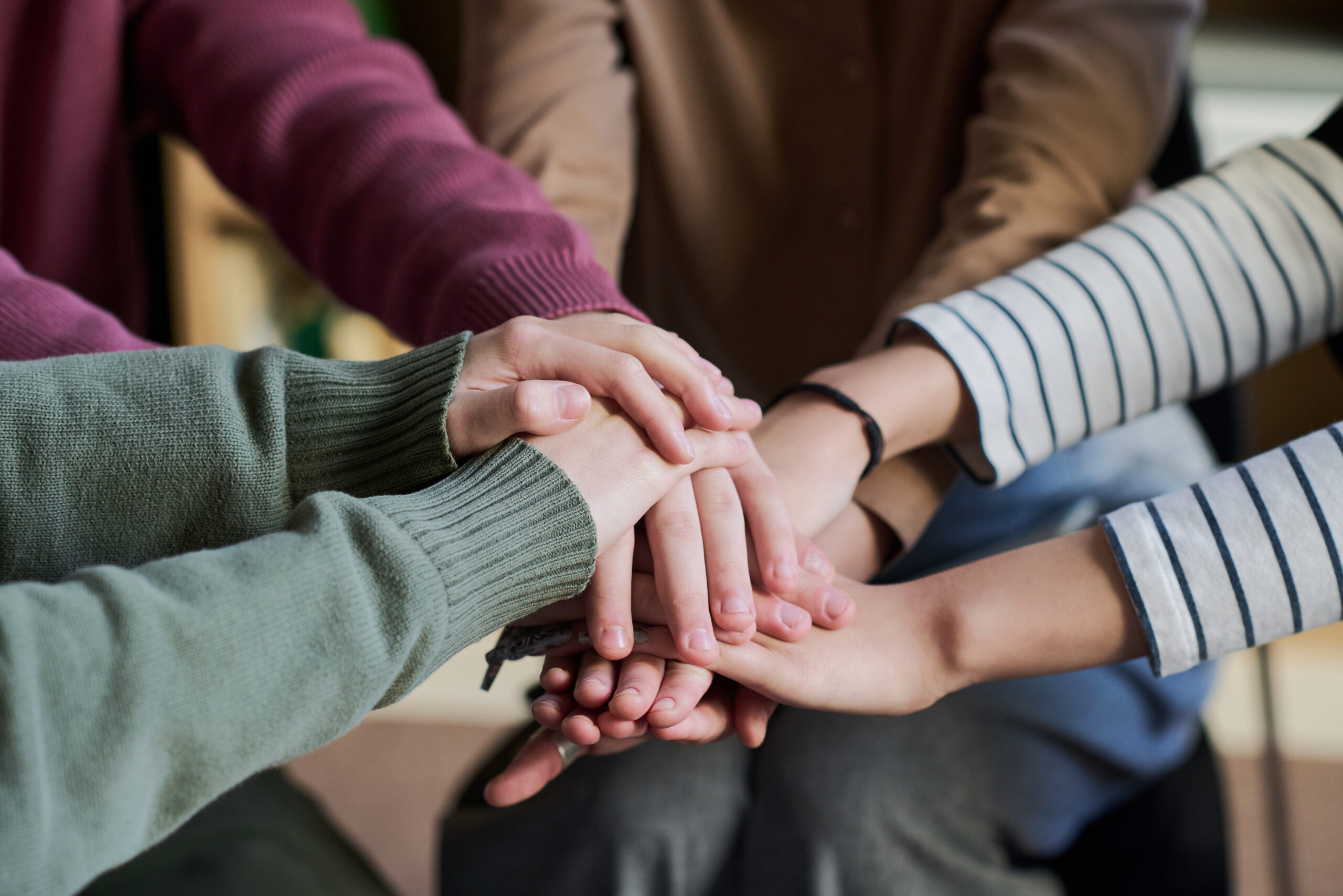Diverse group of young and adult people stacking hands in gesture of unity during group therapy session, multiethnic people supporting each other in teamwork